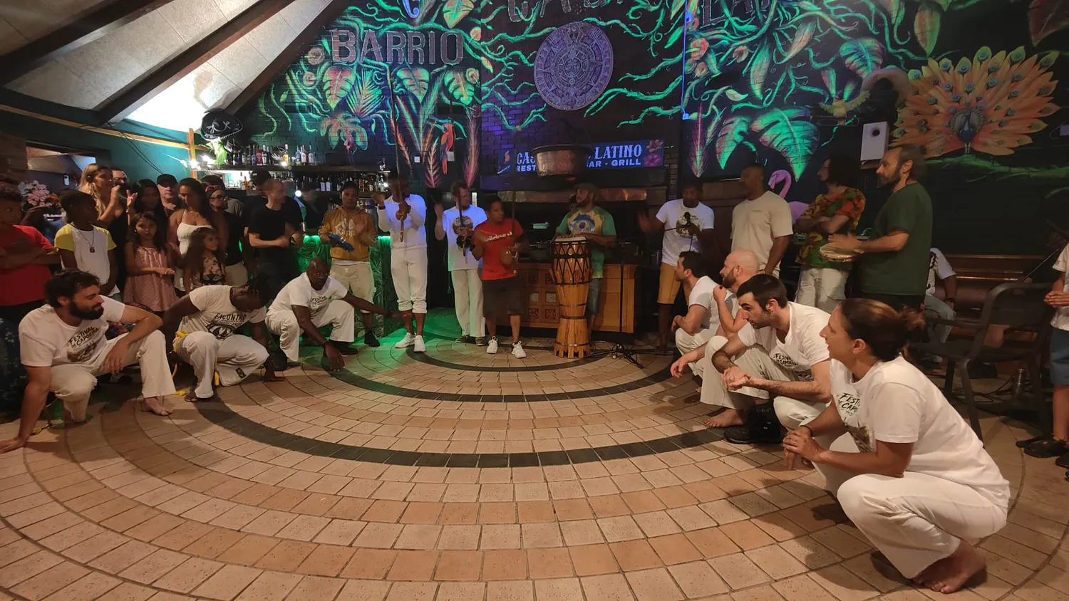 Une roda conviviale entourée de musiciens et de participants devant une fresque colorée