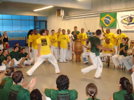 Two capoeiristas in yellow and green T-shirts playing in front of the circle of participants.