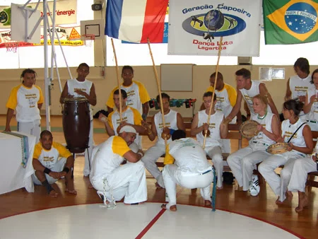 Musiciens au berimbau, au pandeiro et à l’atabaque derrière deux participants accroupis.