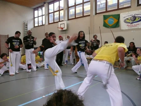 Un capoeirista alza la gamba di fronte al suo compagno, davanti ai musicisti.