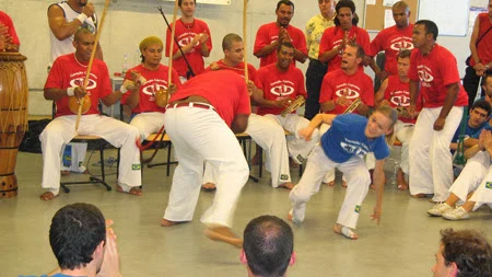 A child in a blue T-shirt playing with an adult, in front of the musicians in red.