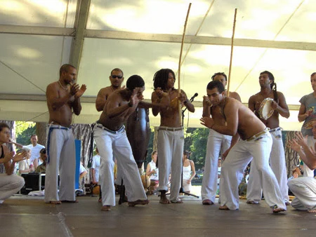 Participants en pantalon blanc réunis sur une scène sous un chapiteau.
