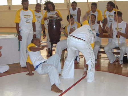 Deux capoeiristes jouent au centre de la roda, l’un proche du sol et l’autre debout.